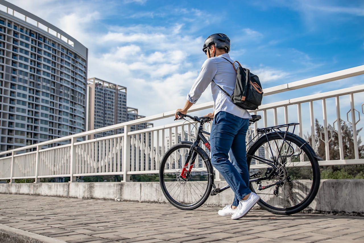 Bărbat cu cască ce își conduce bicicleta în oraș, pe un pod pietonal