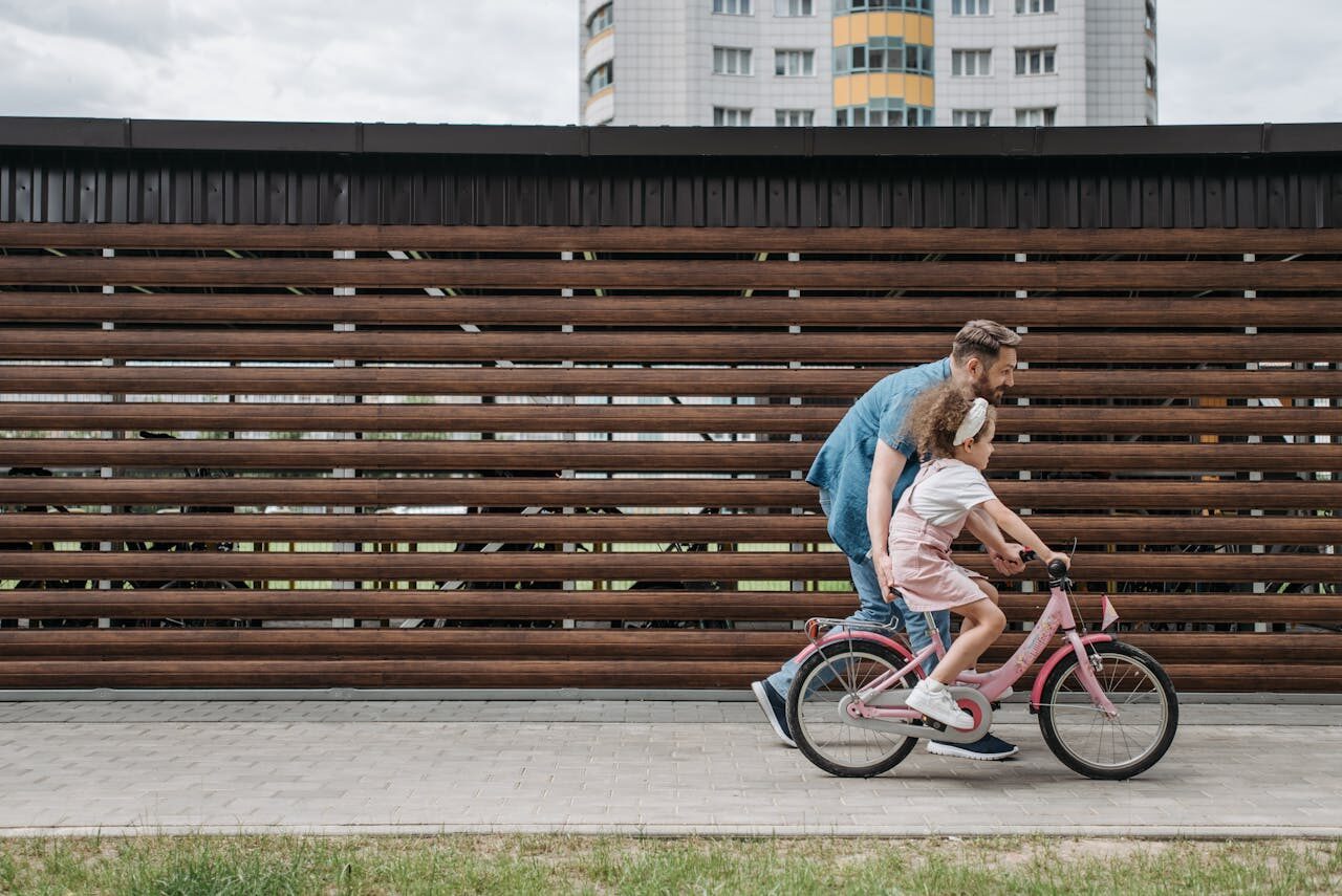 Un tată ce își învață fetița să meargă pe bicicletă pe o alee