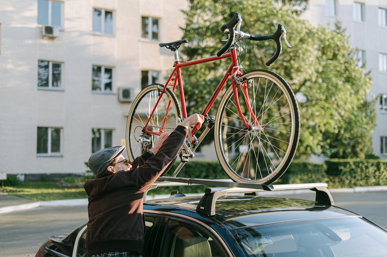 Bărbat fixând o bicicletă roșie pe barele transversale montate pe plafonul unei mașini negre
