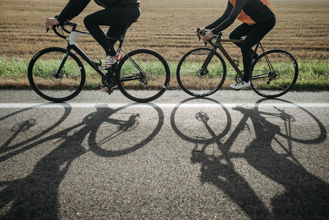 Doi cicliști, surprinși din lateral pedalând pe șosea