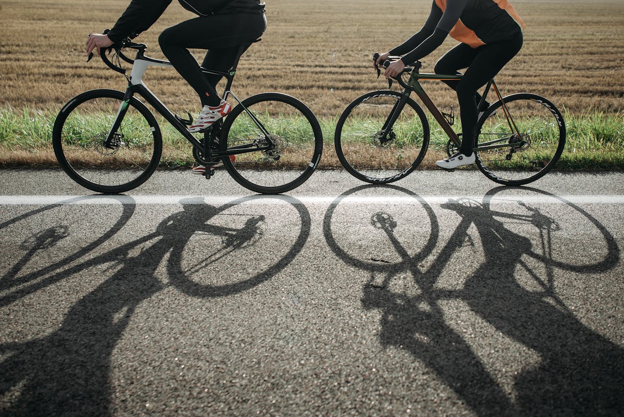 Doi cicliști, surprinși din lateral pedalând pe șosea