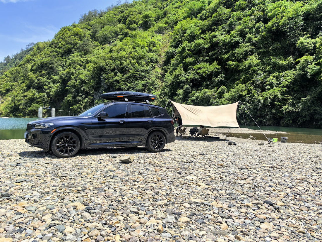 SUV parcat pe malul unui râu, echipat cu o cutie de portbagaj montată pe plafon, ideală pentru călătorii și camping