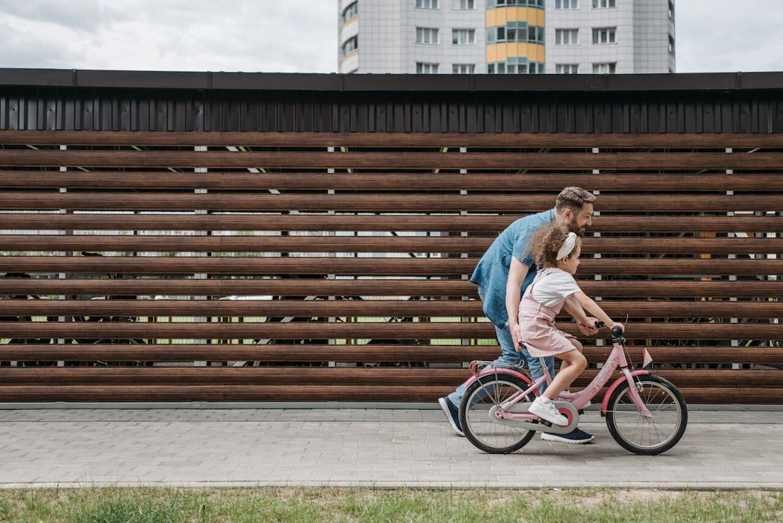 Un tată ce își învață fetița să meargă pe bicicletă pe o alee